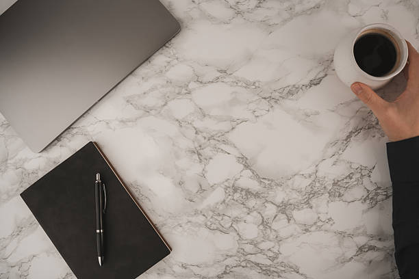 istock A hand holds a coffee cup while a black notebook and pen lie next to a laptop on a marble table. This scene captures a calm morning workspace atmosphere perfect for productivity 2250001988