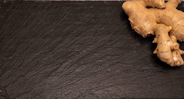 Flat lay of fresh raw ginger root on a black slate stone board with copy space. Healthy spice and herbal medicine ingredient