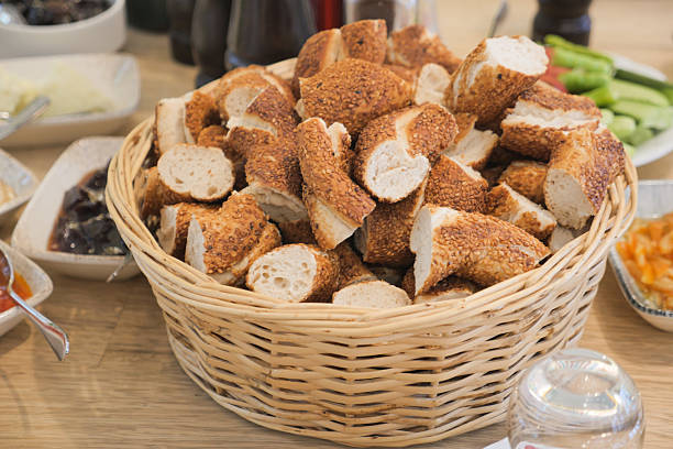 A large basket filled with golden-brown bread rolls sits on a dining table.