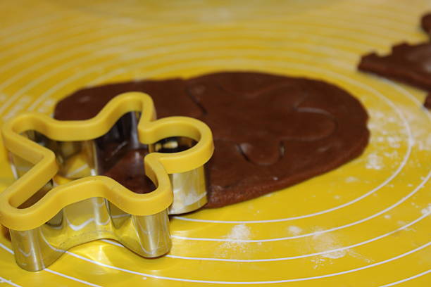 A person is rolling out brown dough on a yellow surface while using a star-shaped cookie cutter. Flour is scattered around from the baking process.