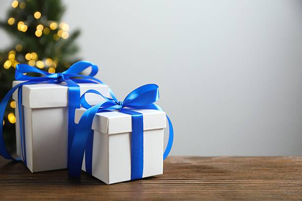 istock Festive gift boxes on the table with shining bokeh and Christmas tree behind 2250019858
