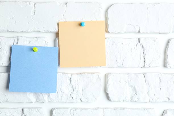 istock Colored paper stickers attached with pushpin on a white brick wall 2250020389