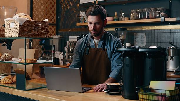 istock Pensive Caucasian staff employee restaurant worker barista guy using laptop ordering products online shopping in Internet male small business owner thinking in cafeteria waiter man type computer cafe 2250020921