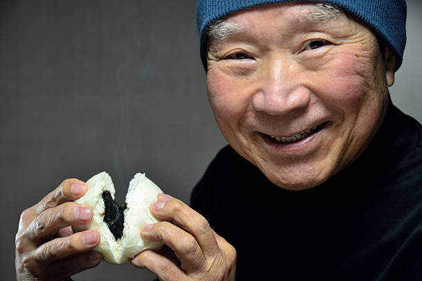 A senior smiling as he eats a steaming steamed bun