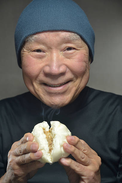 istock A senior smiling as he eats a steaming steamed bun 2250026551