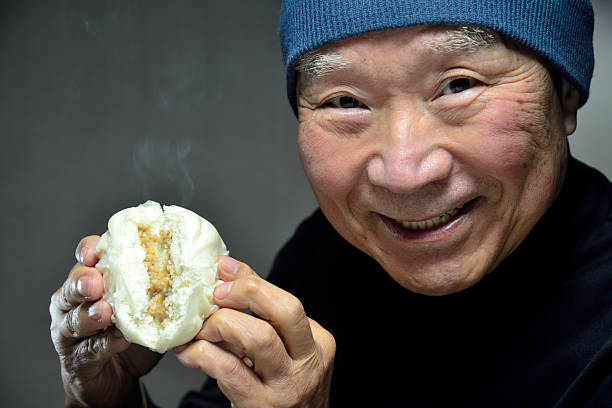 istock A senior smiling as he eats a steaming steamed bun 2250026578