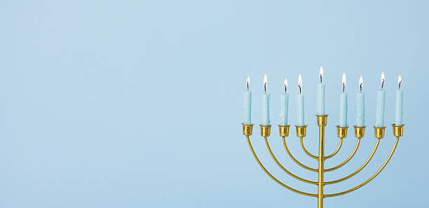 istock A golden menorah with lit candles stands against a soft blue banner backdrop. The image captures Hanukkah celebration, warmth, and greeting moments, conveying tradition, faith, and festive light 2250033702