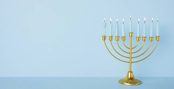 istock A gold menorah with nine candles glows softly on a blue surface, inviting warmth, tradition, faith, and festive spirit for Hanukkah celebration and greeting uses. Elegant and serene decor 2250033713