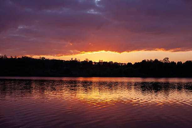 istock Serene lake at sunset with golden reflections on calm water, surrounded by lush trees under a dramatic sky. Perfect for nature and tranquility themes. 2250036794