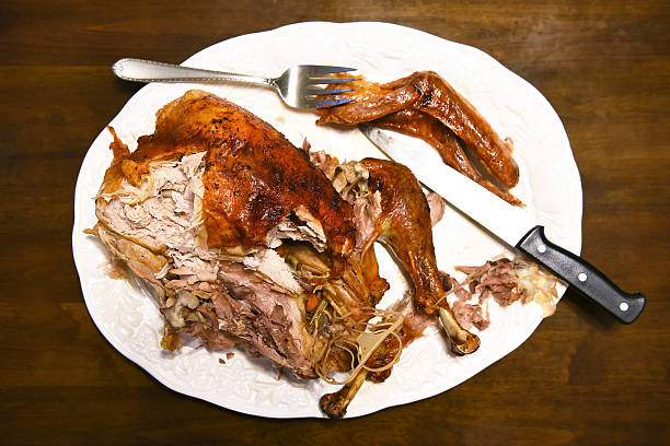 Partially carved Thanksgiving turkey on a white platter with knife and fork on a dark brown table.