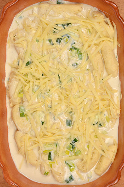 A close-up of potato gnocchi in a creamy leek sauce generously covered with shredded cheese in a ceramic dish, ready for baking
