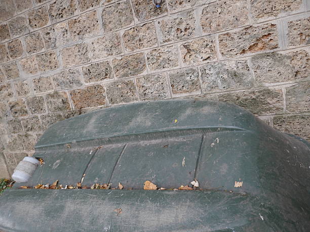 Abandoned old green plastic boat leaning against stone block wall