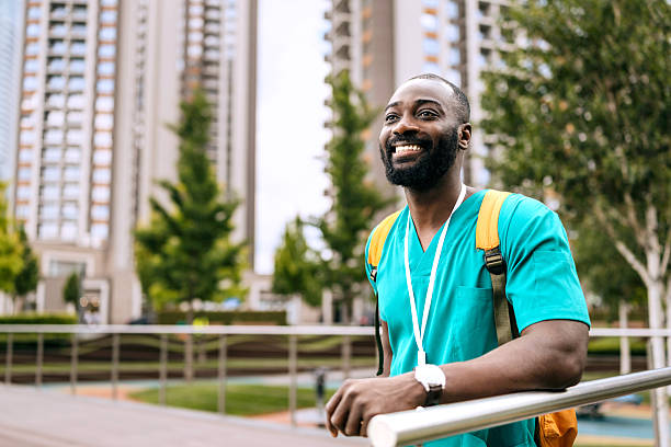 istock Black male nurse smiles while standing outdoors beside a railing in an urban setting with tall buildings and trees 2250048189