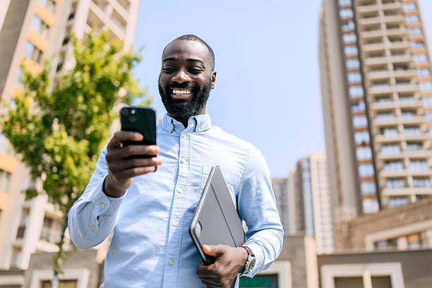 istock Businessman stands outdoors holding a laptop while checking his phone in an urban setting during daytime 2250050097