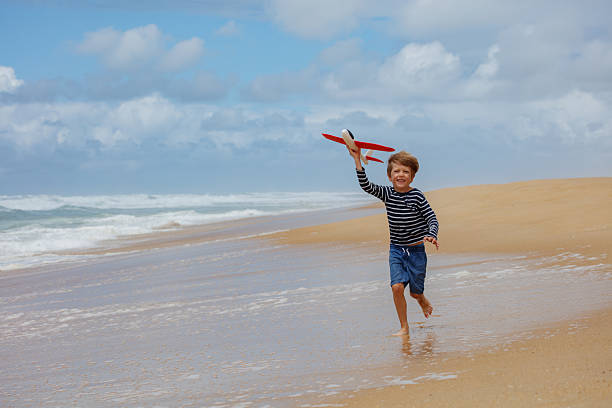 istock Boy kid enjoys beachside fun with toy plane, running on sand 2250058696