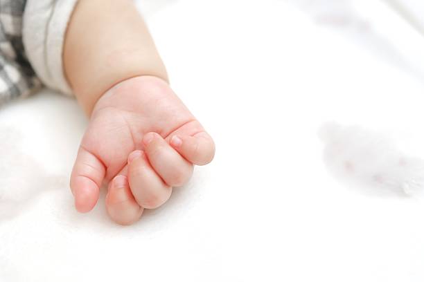 Close-up of a baby's tiny hand resting on a white futon.