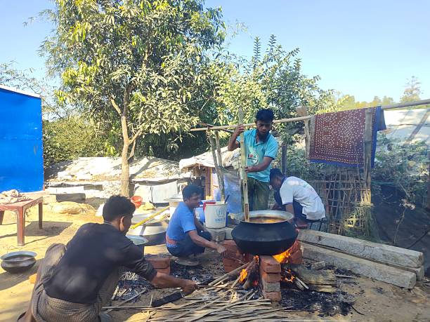 Cox’s Bazar, Bangladesh — Rohingya men prepare a large meal over an open fire inside a makeshift area of the refugee camp on 05 December 2025.