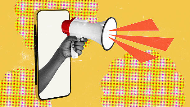 istock Hand holding a megaphone emerges from a smartphone screen on a bright yellow background 2250066832
