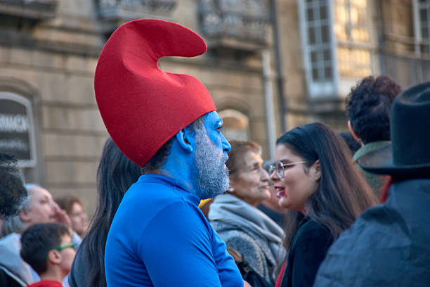 Vigo,Pontevedra,Spain;March 4, 2025:A man dressed as a Smurf stands among the crowd at the vibrant Vigo Carnival in Spain. His face is painted completely blue, and he wears the iconic red hat, capturing the essence of the beloved character. The festival atmosphere is lively, with people enjoying the colorful and creative costumes. This image showcases the fun and imagination present at one of Galicia's most exciting annual celebrations. The detailed Smurf-inspired costume is a perfect representation of carnival spirit, fantasy, and pop culture influences in traditional street festivals.