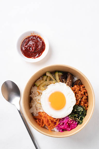 Bibimbap, Korean food, Cooked rice with vegetables, pork and egg in biodegrable bowl and gochujang on white background