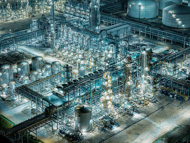 Drone view of a brightly illuminated chemical plant revealing complex pipeline structures at night.