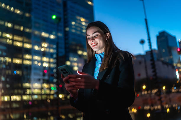 istock Woman smiling using smartphone connecting online in city night 2250078666