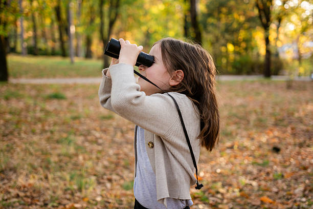 Portrait teenage girl in summer park, holding binoculars in her hands and pointing to the sky, copy space.