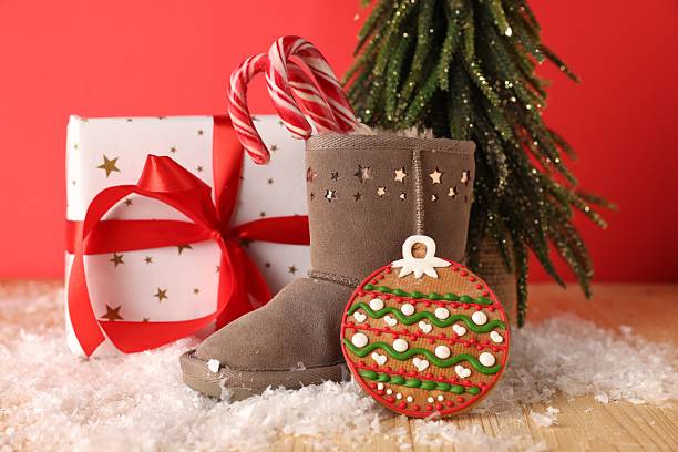 istock Saint Nicholas day. Boot with treats, gift box, fir tree and artificial snow on wooden table against red background 2250080462