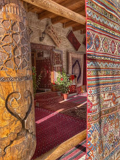 istock Carved wooden column and patterned carpet curtain frame a terrace with red oriental carpets, flowering plants, and walls adorned with carpets in a Bukhara shop. 2250081120