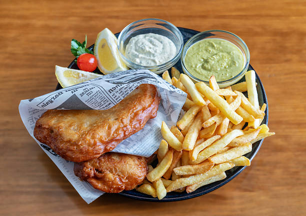 Crispy fish and chips served with fresh lemon, tartar sauce, and green dip on a wooden table, showcasing a delicious meal experience