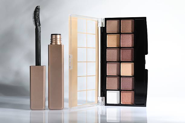 Eyeshadow palette and mascara on mirror surface against white background