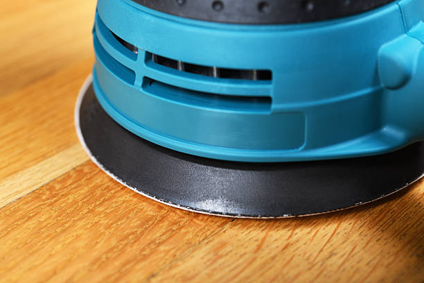 Sanding a wood floor with an orbital sander in a bright room.