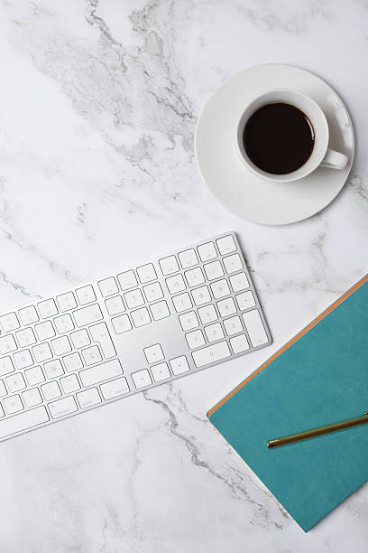 istock Top view vertical of coffee cup, white keyboard and turquoise notebook on marble background, minimalist and soft-toned workspace. Concept of modern workspace and creative lifestyle 2250088803