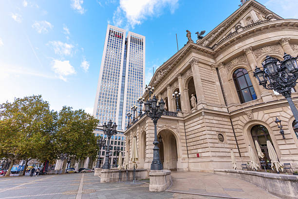 Frankfurt, Germany - October 21, 2025: Frankfurt's historic Alte Oper, with ornate details and lampposts, beautifully contrasts a sleek modern skyscraper. A dynamic urban scene under a bright sky.