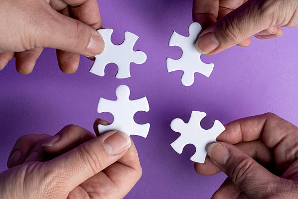 istock Four hands holding white puzzle pieces together on purple background symbolizing teamwork and collaboration 2250098502