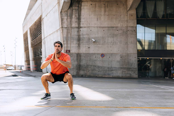 Man performs squats outdoors in a park, wearing athletic clothing