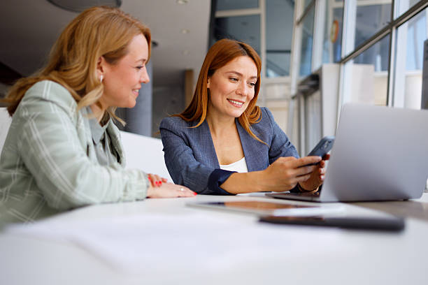 istock Two smiling businesswomen collaborating during office meeting, using laptop and smartphone for innovative ideas 2250105794