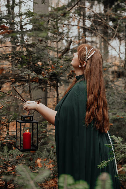 Woman touches branches while standing in a forest wearing a green cloak.