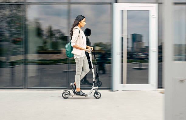 Indian businesswoman energetically commuting to work on a push scooter near a sleek glass building, exuding confidence and focus while navigating the urban landscape.