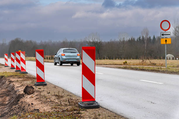 istock Car Passing Road Construction Warning Barriers on Rural Highway Under Cloudy Sky 2250122434