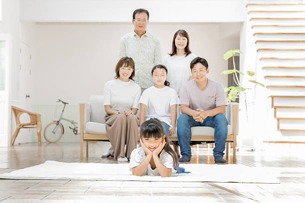 Exhausted tired young parents sitting on floor in the living room while energetic kids boy and girl playing and having fun during weekend together at home. Family leisure and problems in parenthood.