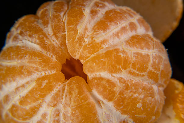 Macro close-up of a peeled mandarin showing juicy citrus texture and natural fibers on a dark background. Fresh orange citrus fruit concept for healthy eating, vitamin C, nutrition and health.
