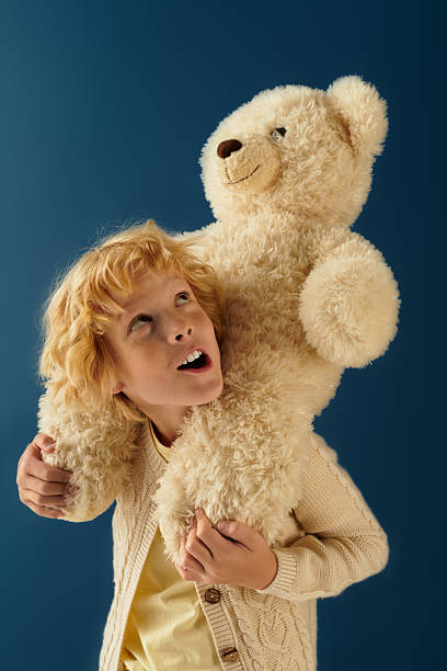 istock Blonde boy embracing a large plush bear against a calming blue backdrop 2250132204
