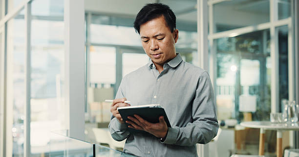 istock Asian man, stylus and tablet in office for research, editing article and schedule update of draft. Person, digital and review for breaking news, proofreading story and interview notes for publication 2250132261