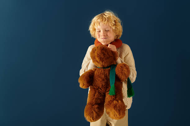 istock Blonde boy smiles joyfully while holding a soft toy against a blue backdrop 2250132376