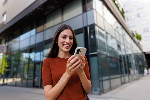 istock Young woman smiling, texting on phone while walking in city, connecting with mobile technology 2250132503