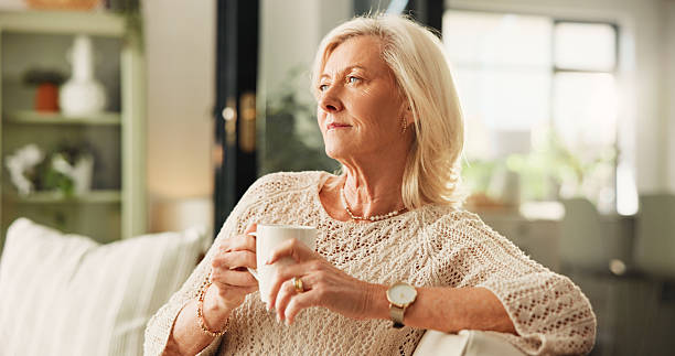 istock Thinking, coffee and senior woman on sofa in home with nostalgia, memory or reflection in morning. Relax, ideas and elderly female person drinking tea in living room for retirement in apartment. 2250134360