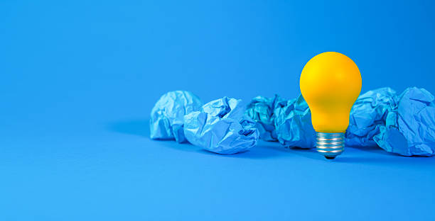 istock yellow light bulb and crumpled paper balls on blue background, idea concept 2250135496
