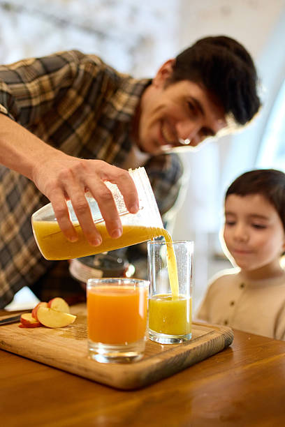 istock Yellow smoothie poured into glass by father with son watching in warm kitchen light 2250138086
