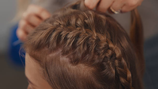 istock Skillful hands effortlessly braiding a young woman's long shiny dark blond hair 2250139264